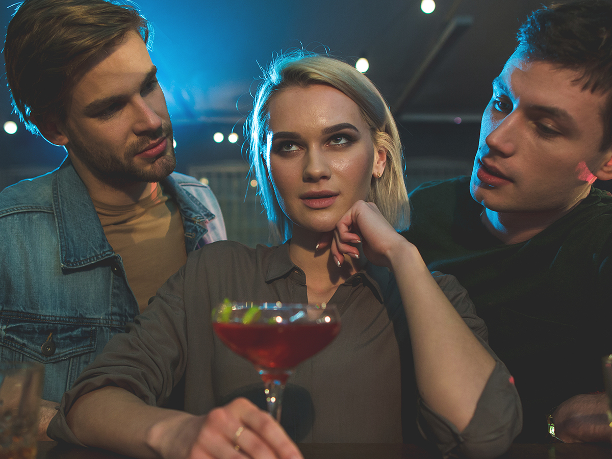 Woman annoyed by two men at a bar.